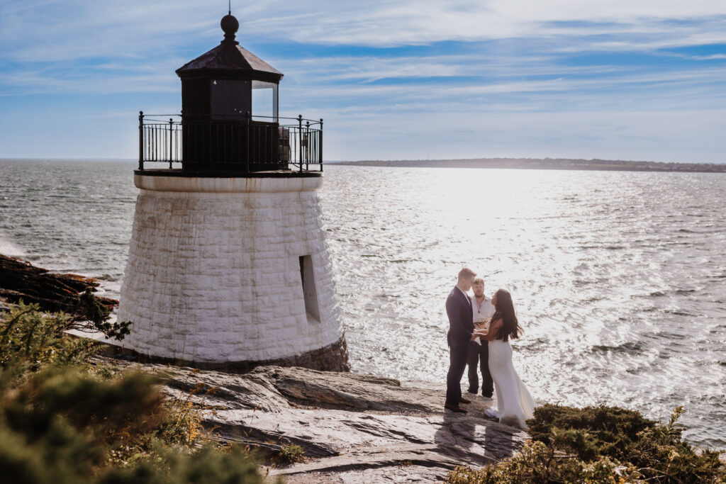 A couple and officiant standing before a seaside lighthouse  wedding location