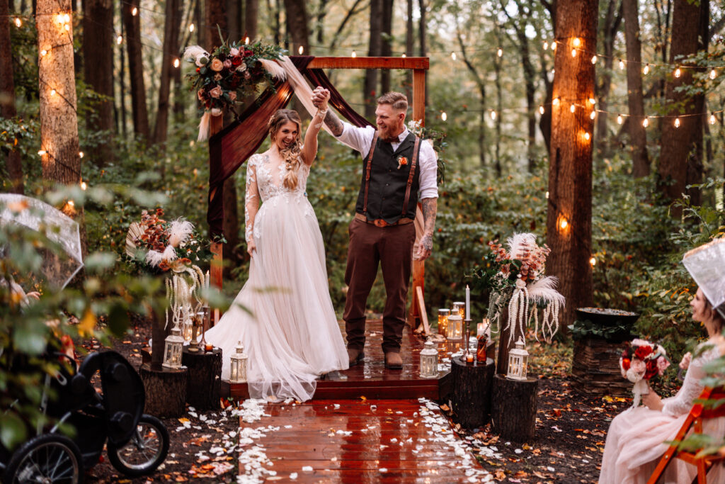 A photograph of a bride and groom standing at a rustic wedding alter.