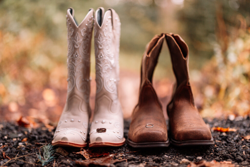 A photo of his and hers cowboy boots with wedding bands balanced on the toes. 