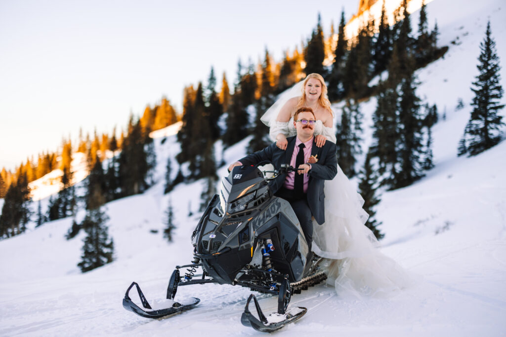 Bride and groom riding a snowmobile on a snowy mountain.