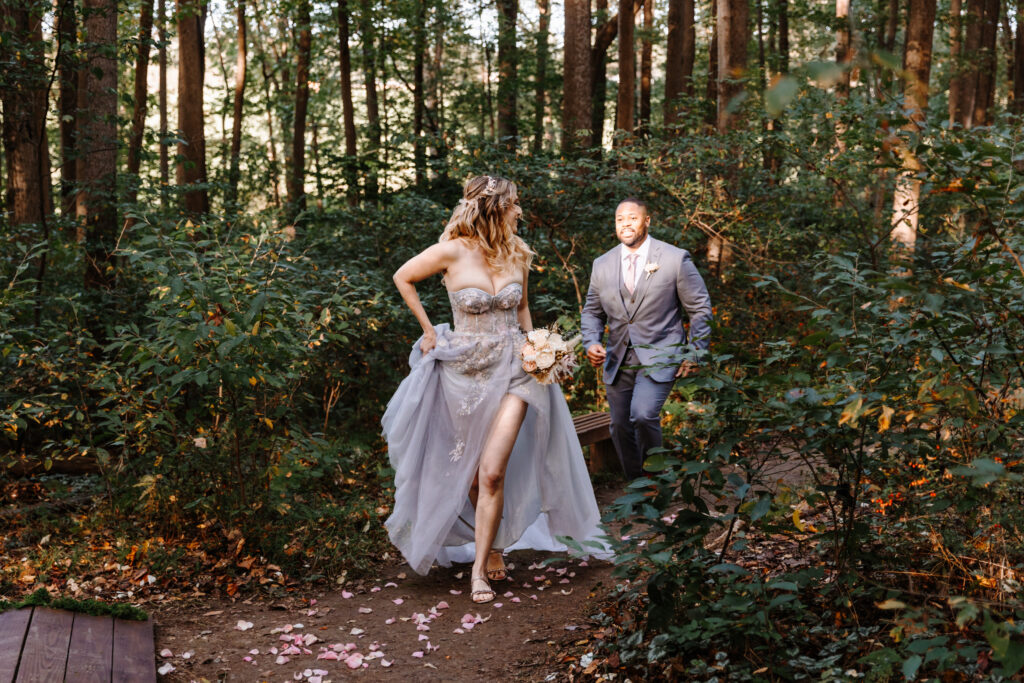 Non-traditional bride and her groom running through the forest