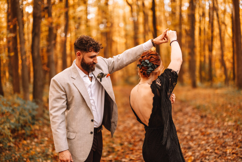 Groom spins bride in a black dress in a beautiful autumn forest. 