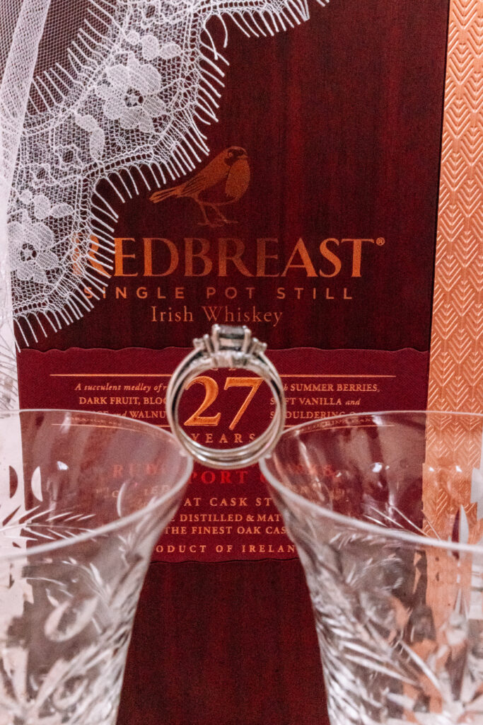 A bottle of fancy Irish whisky behind two crystal glasses and an engagement ring. 