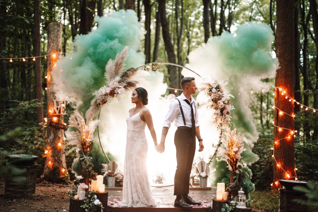 Bride and Groom in front of a beautiful wedding arch backlit with a green smoke bomb. 