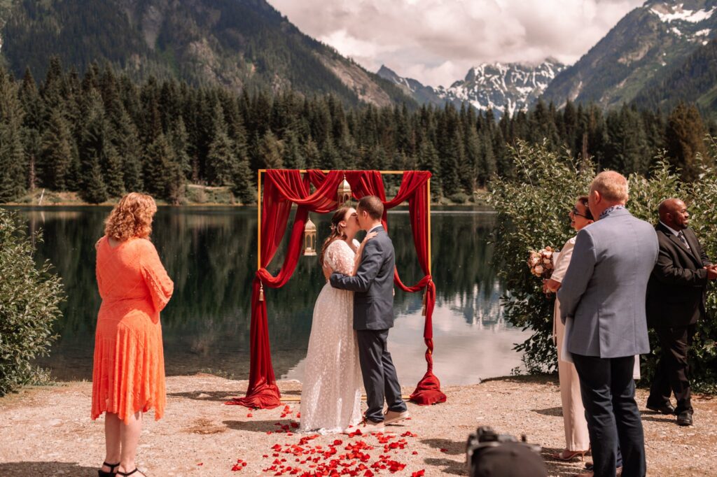 Couple getting married beside a lake as two guests look on clapping. 