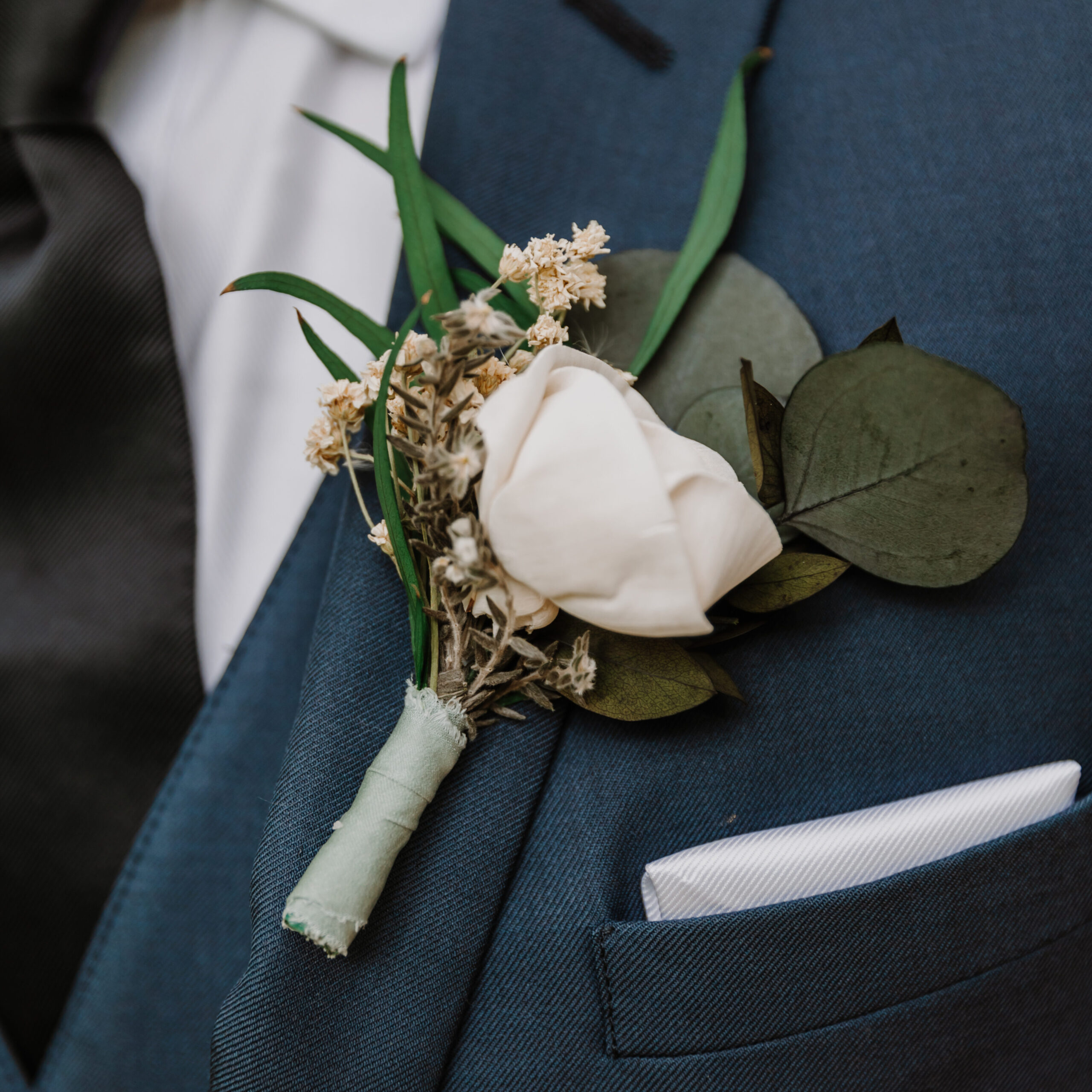 Detail shot of a Groom's boutonniere mad of one small spray rose and dried greenery.