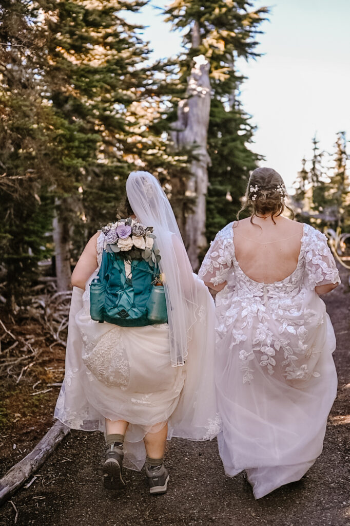 Two brides in wedding gowns hiking to their elopement vista.